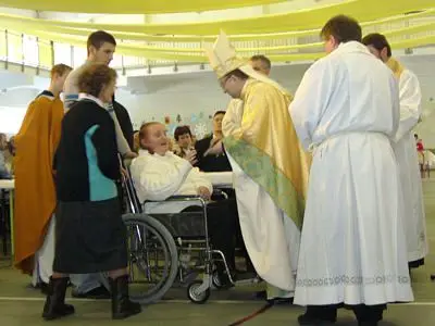 Biskup przyjmuje dary od kobiety na wózku inwalidzkim